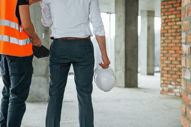 Vue éloignée Homme en costume et bricoleur en vêtements de protection orange travaille sur la construction