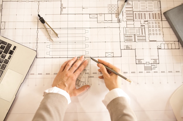 Vue d'ensemble des mains de l'ingénieur avec un crayon faisant un croquis sur le plan tout en utilisant une règle et des diviseurs