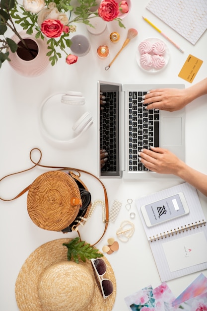 Vue d'ensemble des mains de jeune femme ou femme d'affaires sur le clavier d'ordinateur portable entouré de divers objets