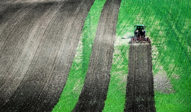 Vue ensoleillée du gros tracteur labourant le sol du champ vert