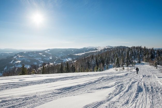 Vue envoûtante sur la piste de ski avec une belle vue sur la forêt de conifères de la colline enneigée et les chaînes de montagnes ensoleillées par une journée claire et glaciale. Concept de détente dans une station de ski. Place pour le texte