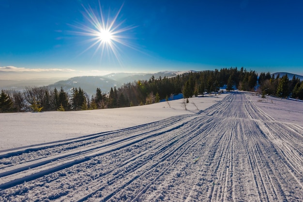 Vue envoûtante de la piste de ski avec une belle vue sur la forêt de conifères de la colline enneigée et les chaînes de montagnes ensoleillées par temps clair et glacial. Concept de détente dans une station de ski. Place pour le texte