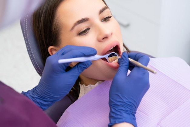 Vue sur l'épaule d'un dentiste examinant les dents d'une patiente dans un cabinet dentaire