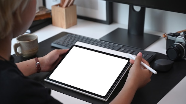 Vue sur l'épaule de la jeune femme tenant une maquette de tablette numérique avec écran blanc au bureau.