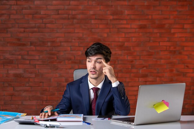 vue de face d'un bel homme d'affaires stressé assis derrière son lieu de travail avec un ordinateur portable en costume plan de travail entrepreneur métier constructeur travail d'entreprise projet d'entreprise