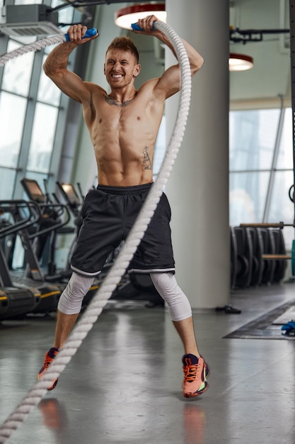 Photo vue de face d'une belle jeune sportive en forme et tonique travaillant avec des cordes de combat