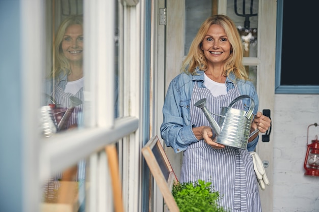 Vue de face d'une botaniste souriante tenant un arrosoir galvanisé à deux mains