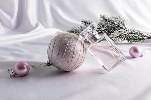 La vue de face d'une bouteille de parfum féminin sur fond d'une belle boule de Noël et d'une présentation d'arôme de fond de satin blanc