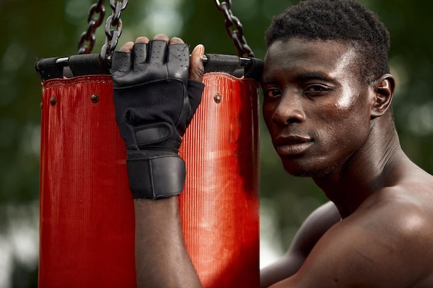 Vue de face d'un boxeur noir musclé frappant vers la caméra avec un visage profond et intense Concept de boxe et d'entraînement en plein air