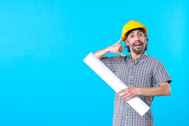 Vue de face constructeur masculin en casque jaune avec plan sur fond bleu architecture du bâtiment constructeur d'emplois ingénieur ouvrier immobilier