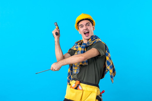 Vue de face constructeur masculin en casque tenant un tournevis et un marteau sur fond bleu constructeur de construction d'emplois de maison plate