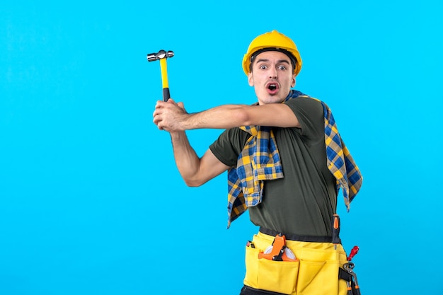 vue de face constructeur masculin se préparant à frapper avec un marteau sur fond bleu travail de la maison constructeur bâtiment plat