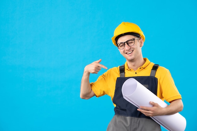 Vue de face constructeur masculin en uniforme avec plan papier sur bleu