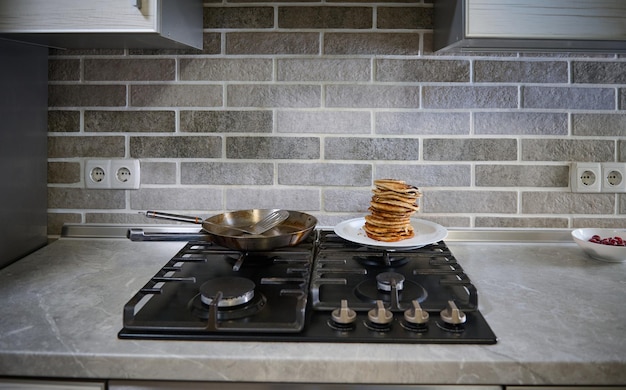 Vue de face de crêpes maison fraîchement cuites sur plaque blanche, poêle à frire en acier et spatule sur un poêle noir dans la cuisine à domicile. Notion de mardi gras