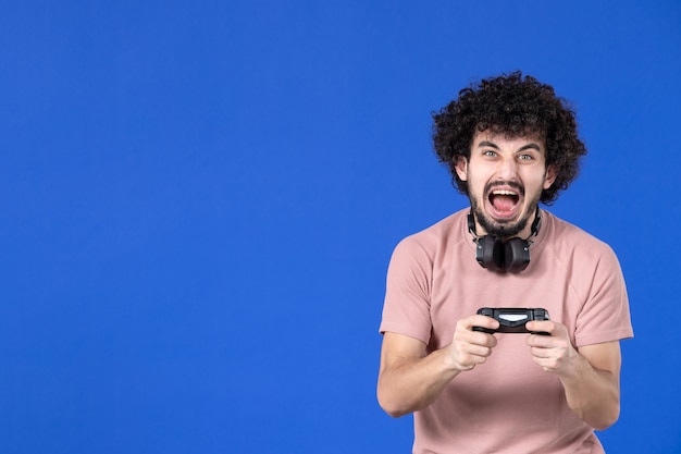 vue de face crier joueur masculin jouant à un jeu vidéo avec manette de jeu sur fond bleu football adulte joie canapé joueur virtuel adolescent jeune jeunesse gagnant