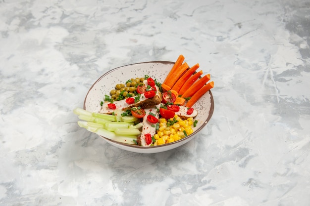 Vue de face d'une délicieuse salade avec divers ingrédients sur une assiette sur une surface blanche avec espace libre