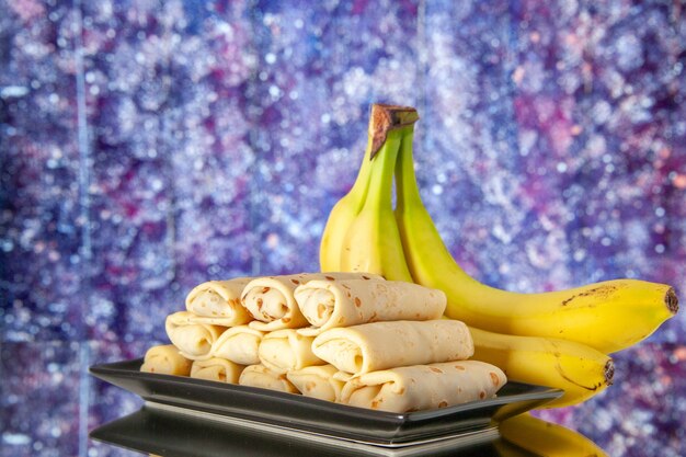 Photo vue de face délicieux crêpes roulées avec des bananes sur fond violet clair matin couleur lait petit déjeuner dessert gâteau sucré sucre