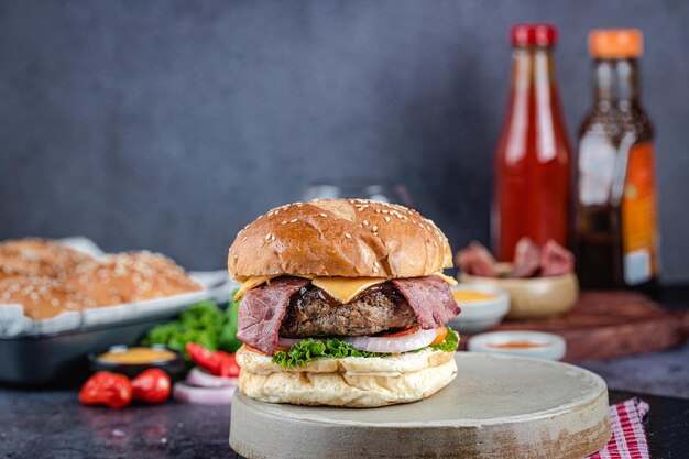 Vue de face d'un délicieux hamburger au fromage et à la viande et au bacon avec de la salade sur une surface sombre de la planche à découper