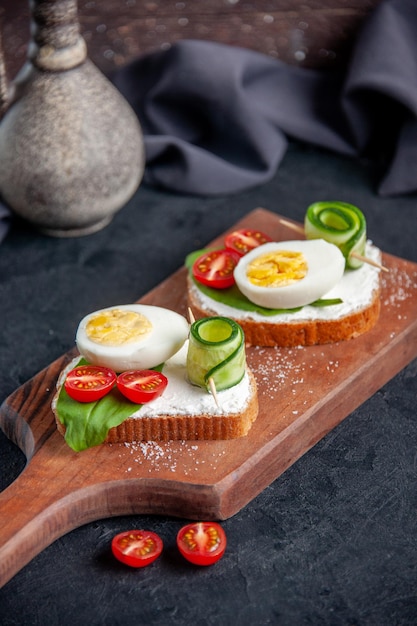 vue de face de délicieux sandwichs aux tomates concombres et œufs sur une planche à découper fond sombre sandwich burger nourriture petit déjeuner toast repas déjeuner