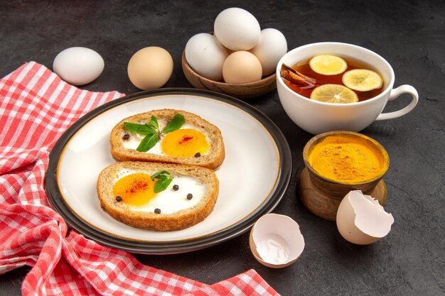 vue de face de délicieux toasts aux œufs avec du thé sur fond sombre repas pain omelette nourriture déjeuner matin petit déjeuner thé