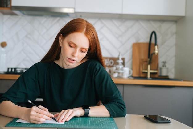 Vue de face d'un dessin de designer féminin concentré faisant une marque avec un crayon sur du papier vierge blanc allongé sur