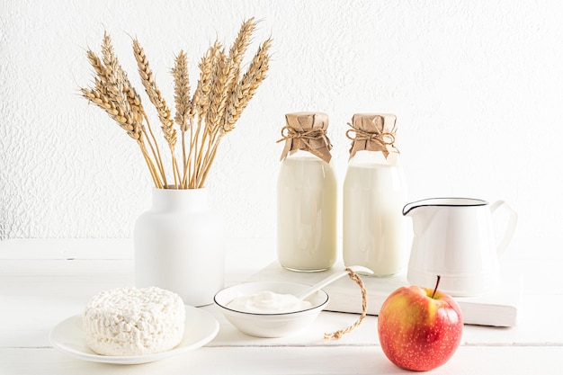 Vue de face de deux bouteilles et un pichet de lait fromage cottage crème sure dans des bols un vase avec des épis de maïs le concept de la fête de Chavouot