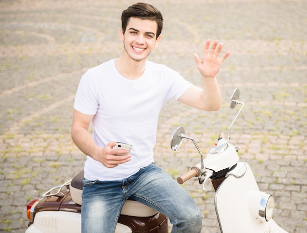 Vue de face du bel homme avec téléphone assis sur le scooter.