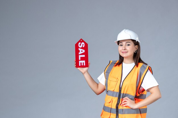 Vue de face du constructeur féminin tenant un tableau de vente rouge sur un mur blanc