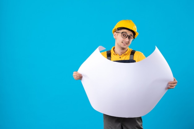 Vue de face du constructeur masculin en uniforme jaune avec plan sur bleu