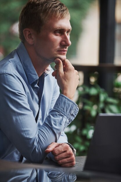 Vue de face du gars qui est dans un café moderne avec son ordinateur portable pendant la journée.