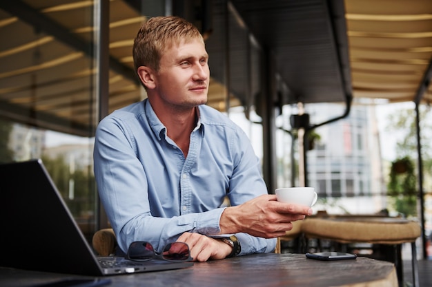 Vue de face du gars qui est dans un café moderne avec son ordinateur portable pendant la journée.