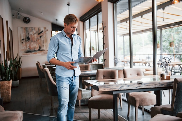 Vue de face du gars qui est dans un café moderne avec son ordinateur portable pendant la journée.