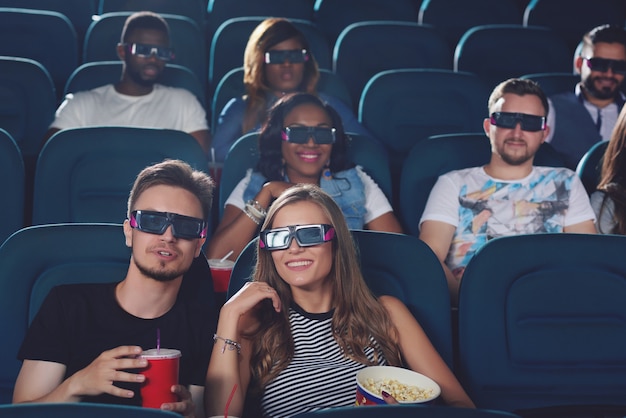 Vue de face du jeune couple parlant au cinéma et regardant un film, tenant une tasse de cola et de pop-corn.