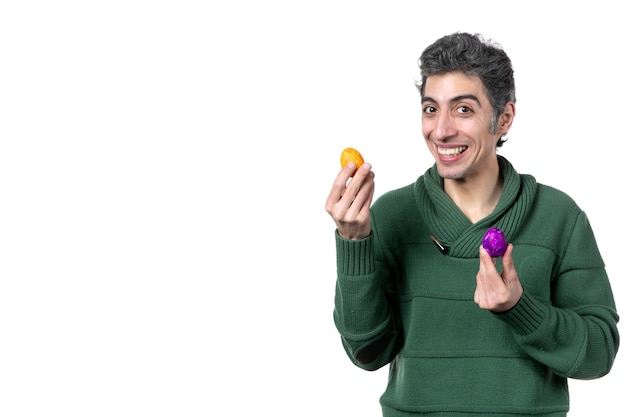 Vue de face du jeune homme souriant tenant des œufs peints de couleur sur fond blanc danseur horizontal concept ethnique couleurs de printemps interprète novruz