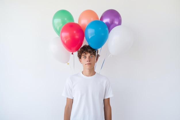 Vue de face du jeune homme tenant des ballons colorés sur un mur blanc