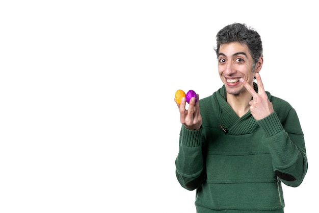 vue de face du jeune homme tenant des œufs peints de couleur sur un mur blanc