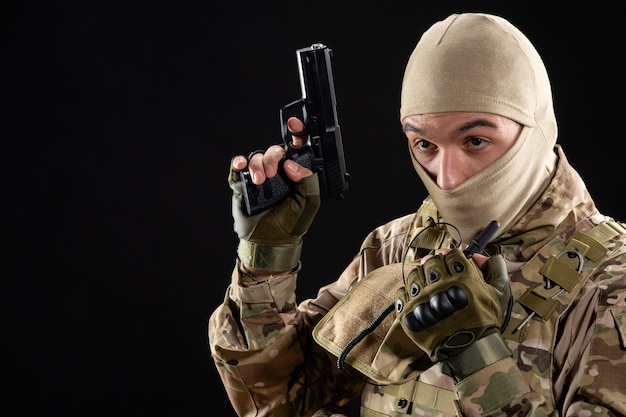 Vue de face du jeune soldat en uniforme avec arme à feu sur le mur noir