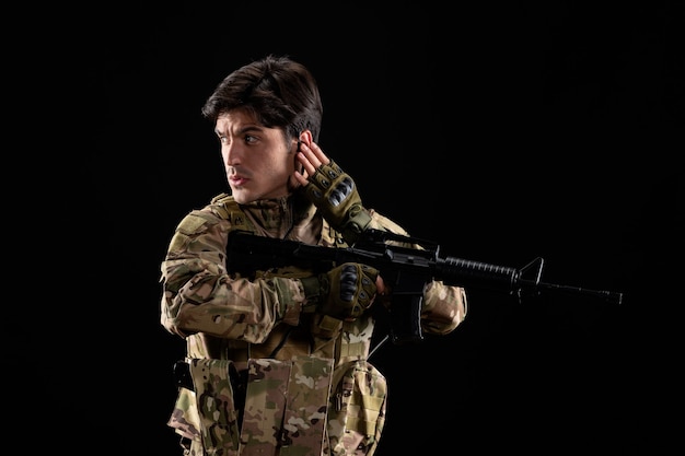 Vue de face du jeune soldat en uniforme avec fusil sur mur noir