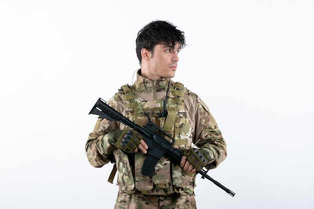 Vue de face du jeune soldat en uniforme militaire avec mur blanc de mitrailleuse