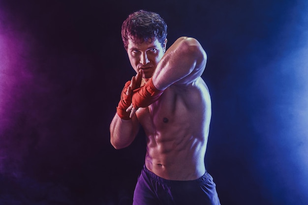 Vue de face du kickboxer musclé qui délivre un coup de coude isolé sur fond de fumée technique mixte