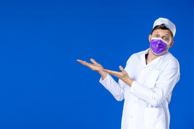 Vue de face du médecin de sexe masculin en costume médical et masque violet parler à quelqu'un de côté sur le bleu