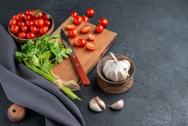 Vue de face du paquet vert de tomates fraîches sur une planche à découper en bois et dans un bol sur une surface noire en détresse