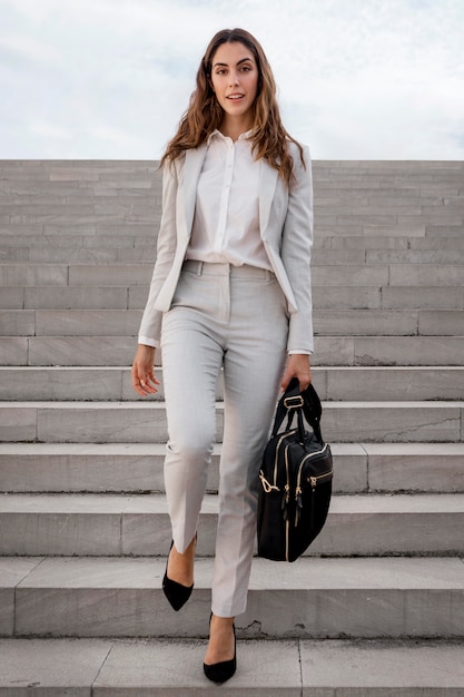 Photo vue de face de l'élégante femme d'affaires dans les escaliers à l'extérieur avec sac