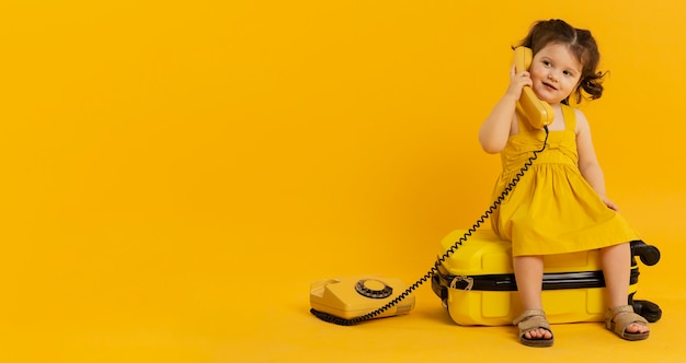 Vue de face d'un enfant mignon posant avec téléphone et bagages