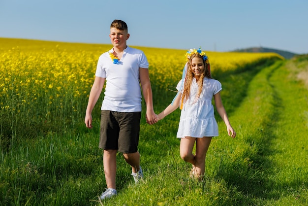 Vue de face des enfants frère et soeur marchant loin le long du chemin avec de l'herbe entourée de champs jaunes