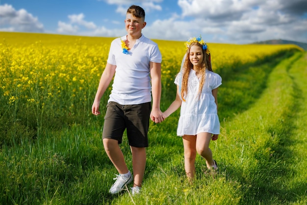 Vue de face des enfants frère et soeur marchant loin le long du chemin avec de l'herbe entourée de champs jaunes