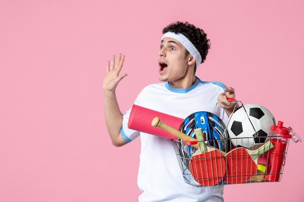 Vue de face excité jeune homme en vêtements de sport avec panier plein de choses sportives