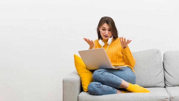 Vue de face d'une femme assise sur un canapé et ne sachant pas ce qui se passe sur son ordinateur portable