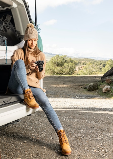 Vue De Face De La Femme Assise Dans Le Coffre De La Voiture Lors D'un Voyage Sur La Route Et Tenant La Caméra