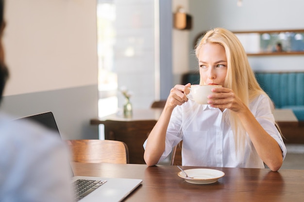 Vue de face d'une femme blonde séduisante et heureuse assise devant un jeune homme méconnaissable à la table de